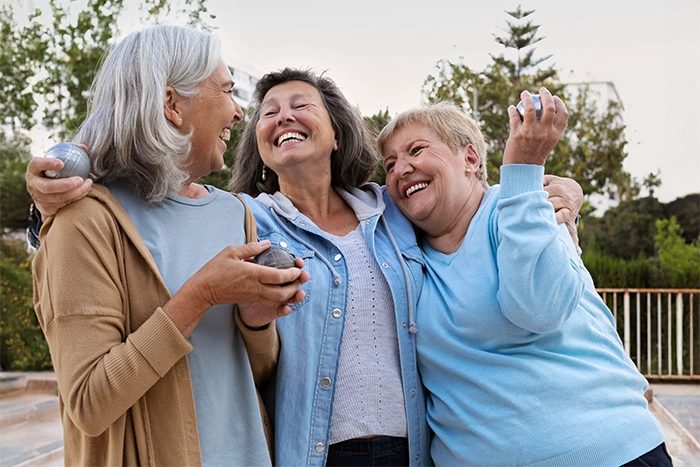Three older women laughing together outdoors, staying active and independent